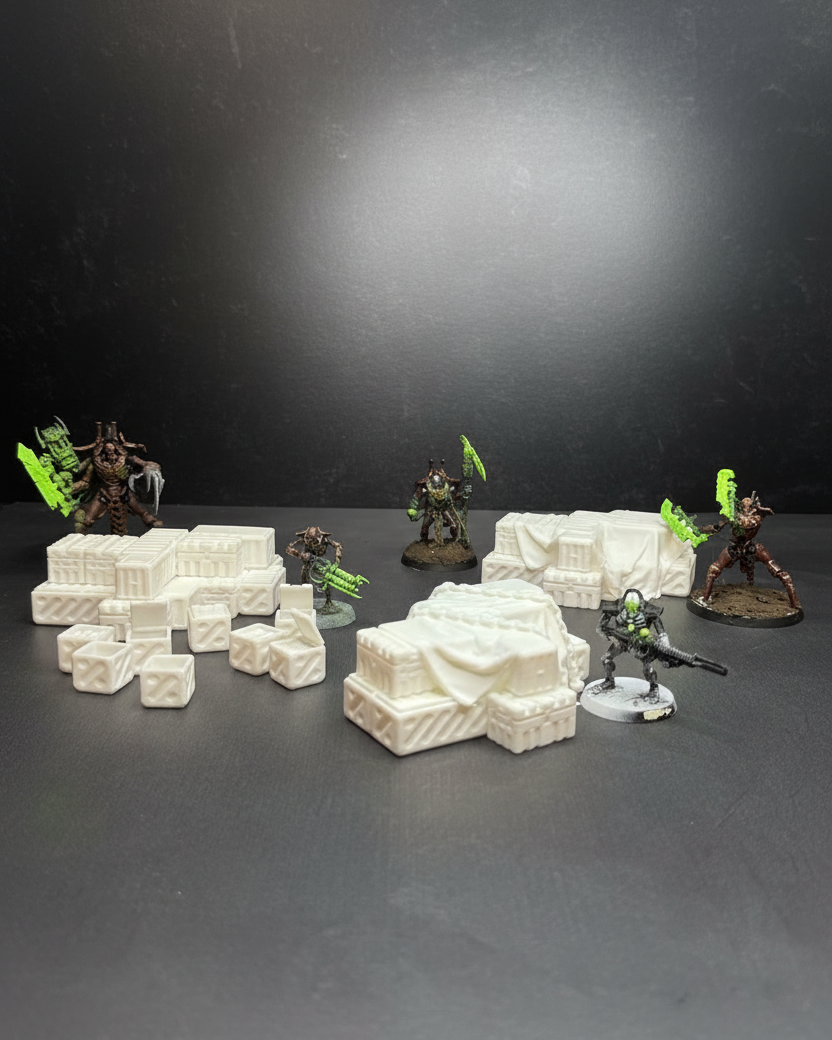 Unpainted sci-fi industrial cargo crates terrain set on dark neutral surface with miniatures shown for tabletop scale reference.